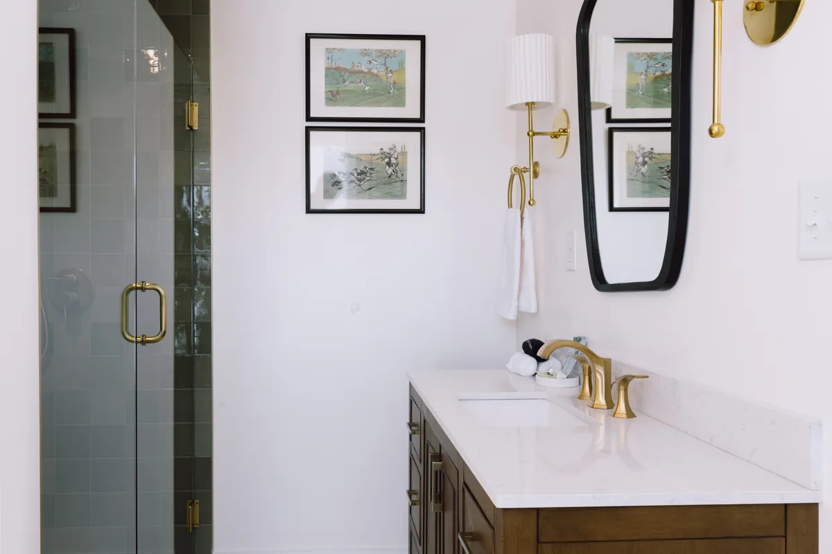 Darwin Room bathroom vanity with brass faucet, framed prints and glass shower door