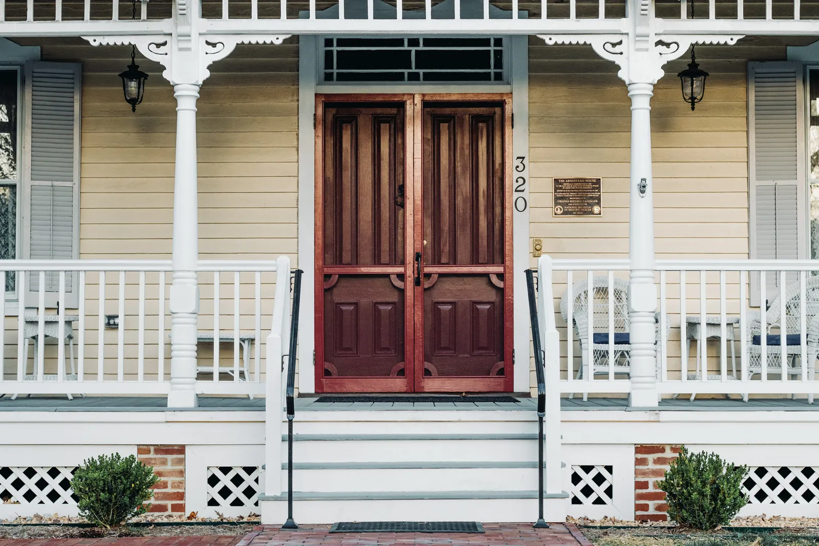 The red double front door, porch, and National Register plaque of Armistead House, an 1890 Victorian inn in Williamsburg, Virginia.