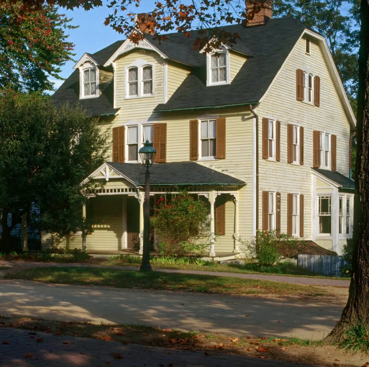 Exterior view of the Armistead House on Duke of Gloucester Street in Colonial Williamsburg, Virginia, showing the Queen Anne Victorian facade with brown shutters and wraparound porch before its 1995 relocation